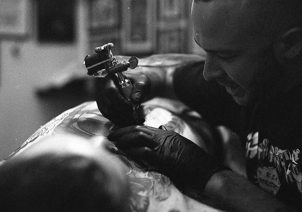 Charlie Lacroix tattooing a chest, black and white photo
